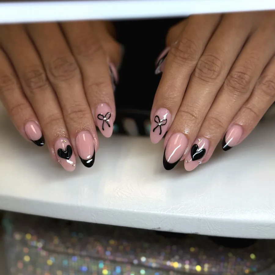 Black French tip almond nails with heart and bow nail art by Legacy Nail Studio, Austin TX
